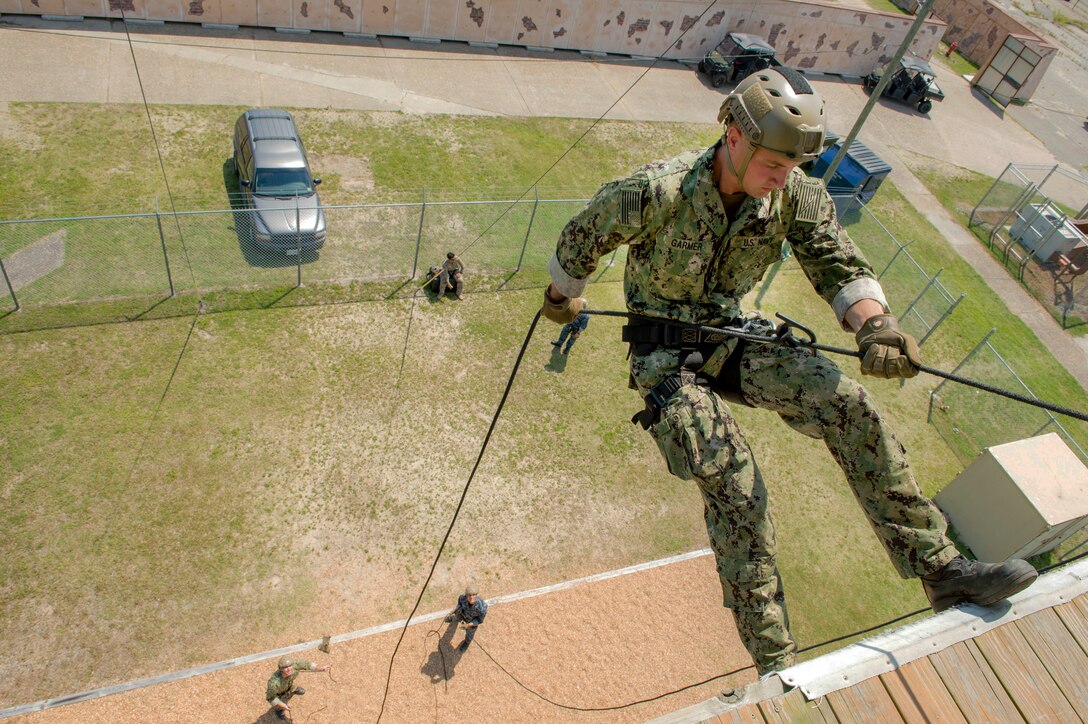 A sailor uses a rope to rappel down a wall.
