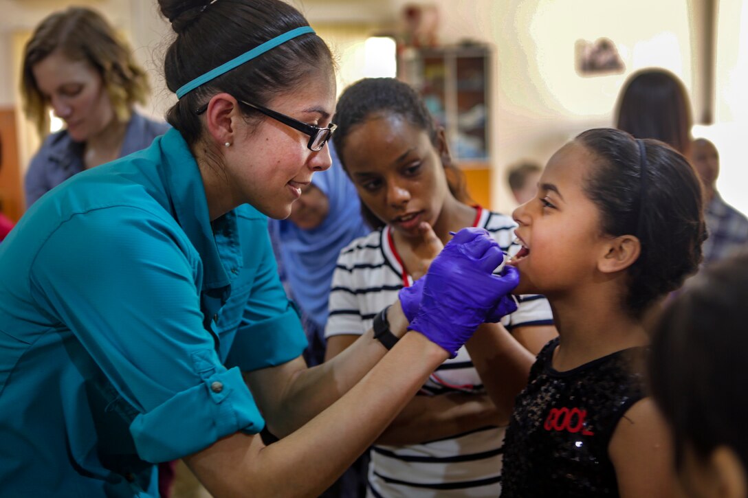 A sailor wearing gloves uses a swab to put fluoride in a child's mouth.