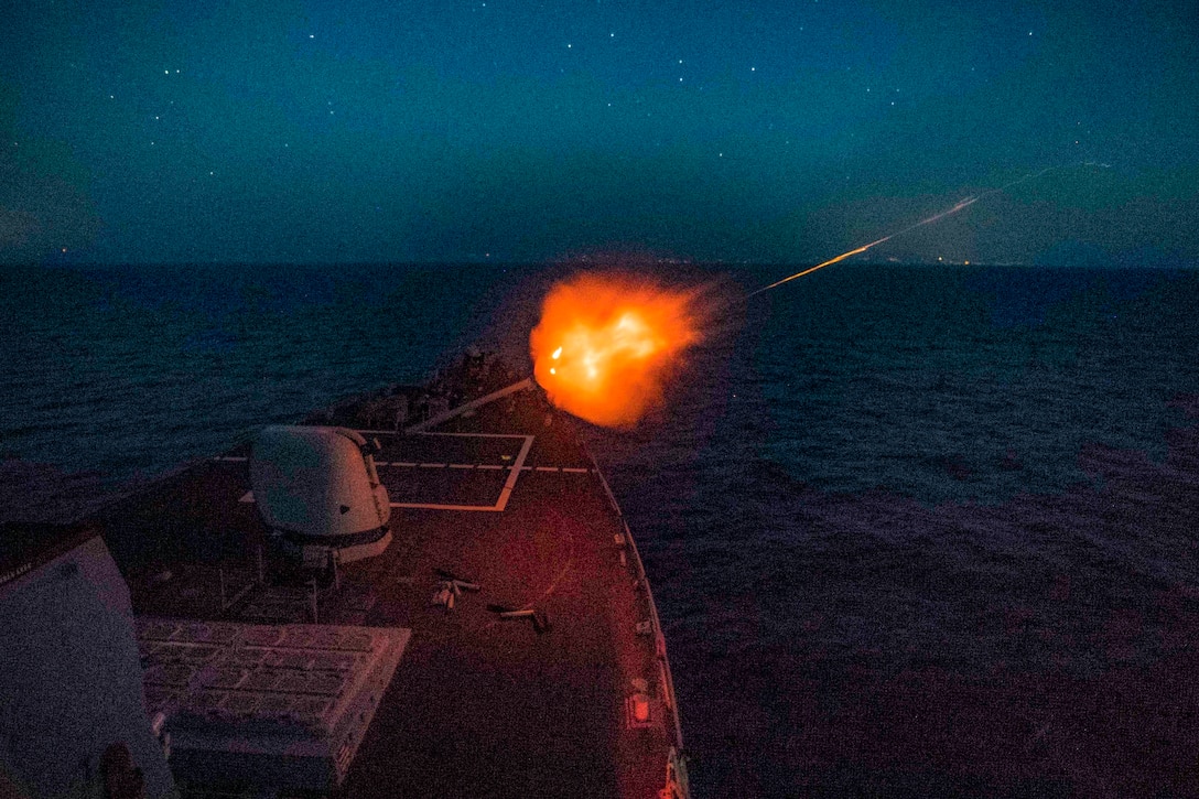 A ship fires a gun at night.