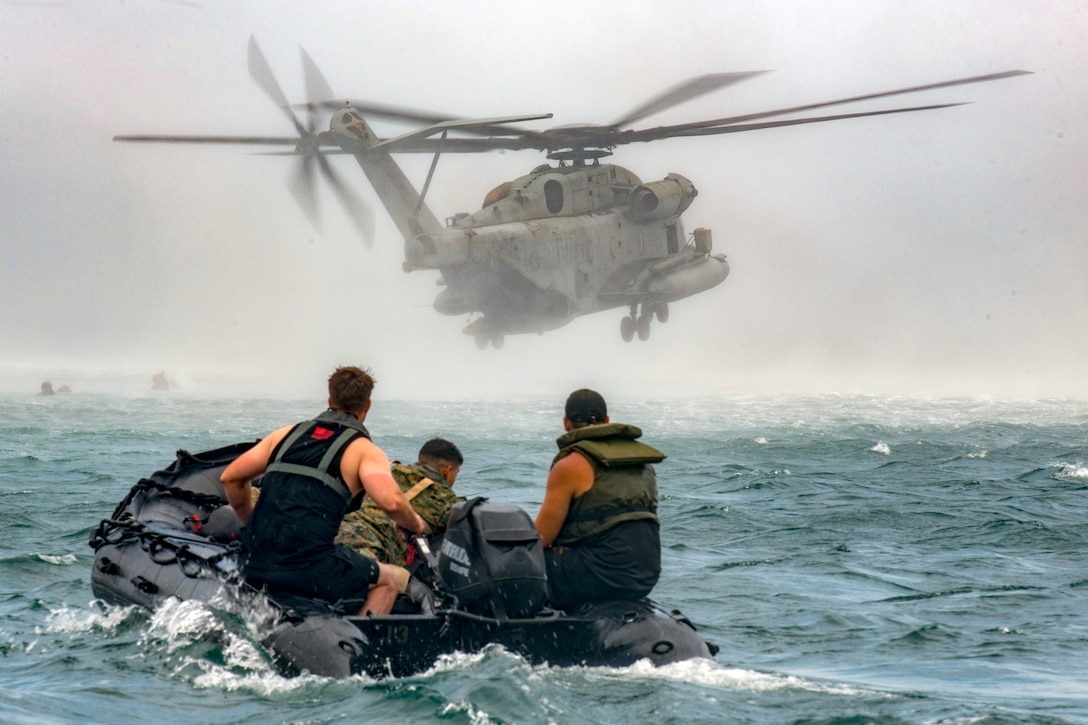 Marines on a small boat head toward a helicopter.