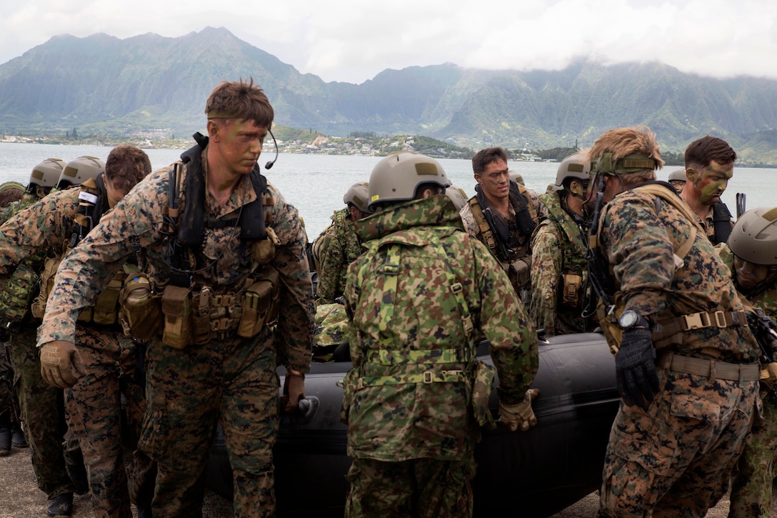 U.S. Marines and Japanese soldiers carry ashore a combat rubber raiding craft.