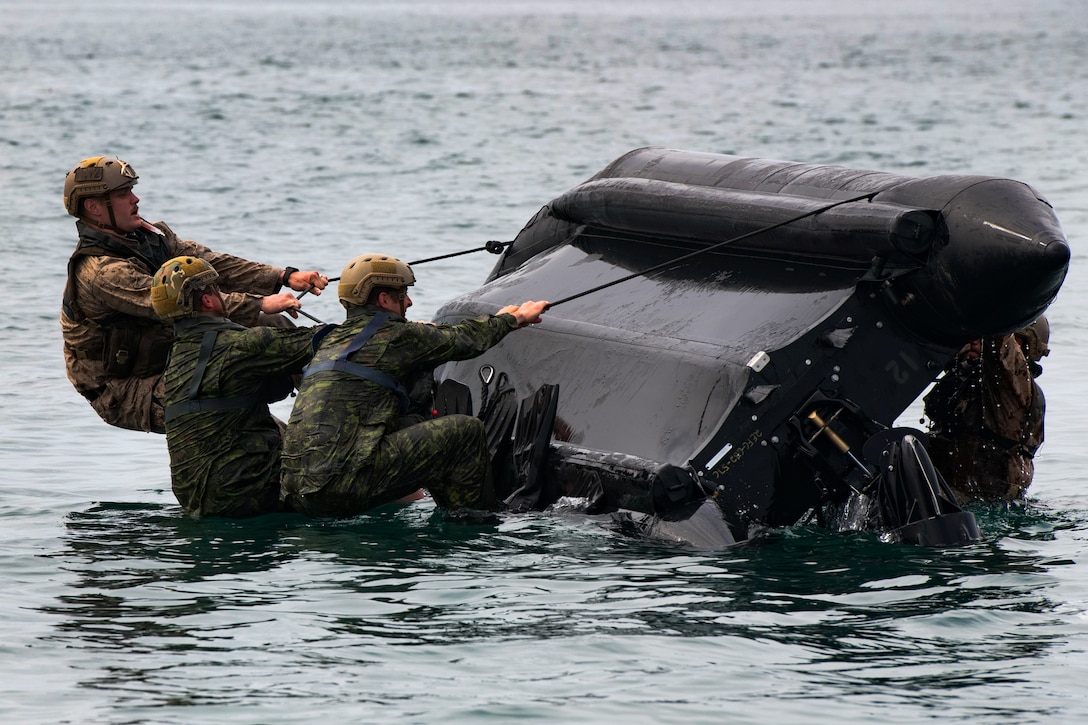 U.S. Marines and Canadian troops attempt to upright a rigid-hull inflatable boat.