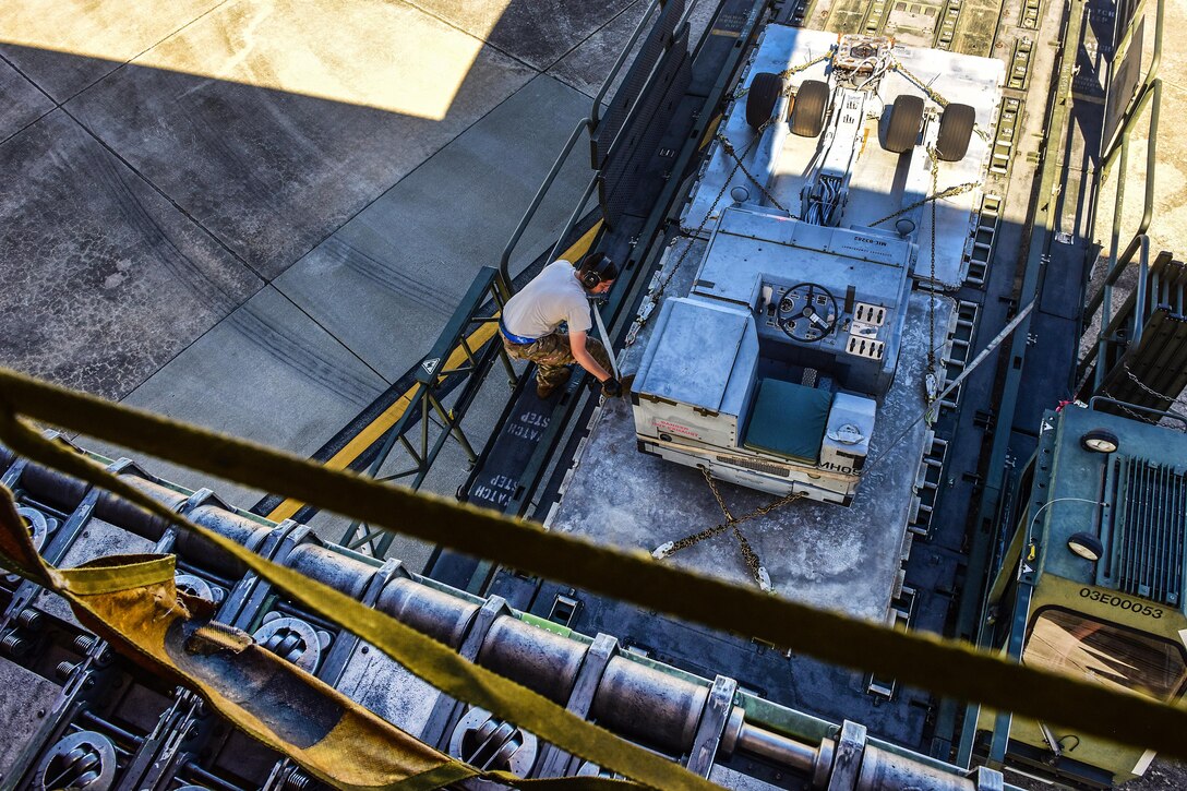 An Air Force airman ensures the cargo straps are secured while loading support equipment and rolling stock cargo.