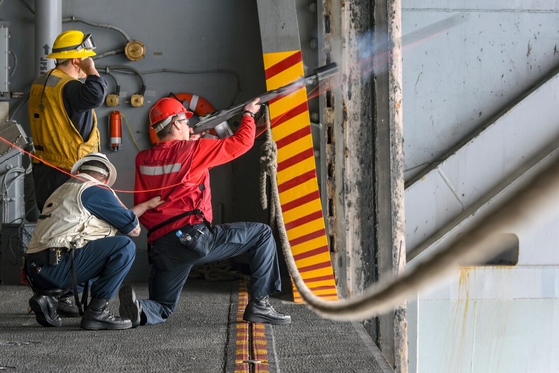 Three sailors kneel on the edge of a ship.