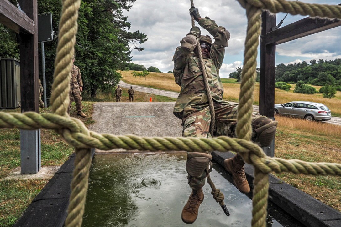 A soldier swings over water using a rope.
