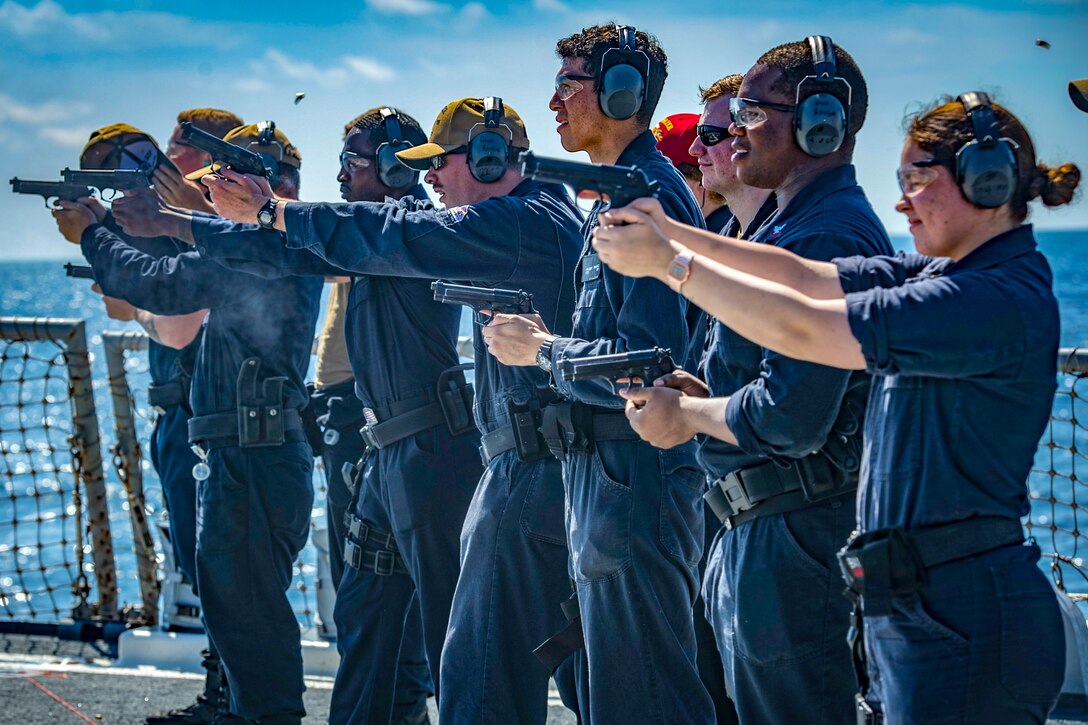 A line of sailors fire handguns.