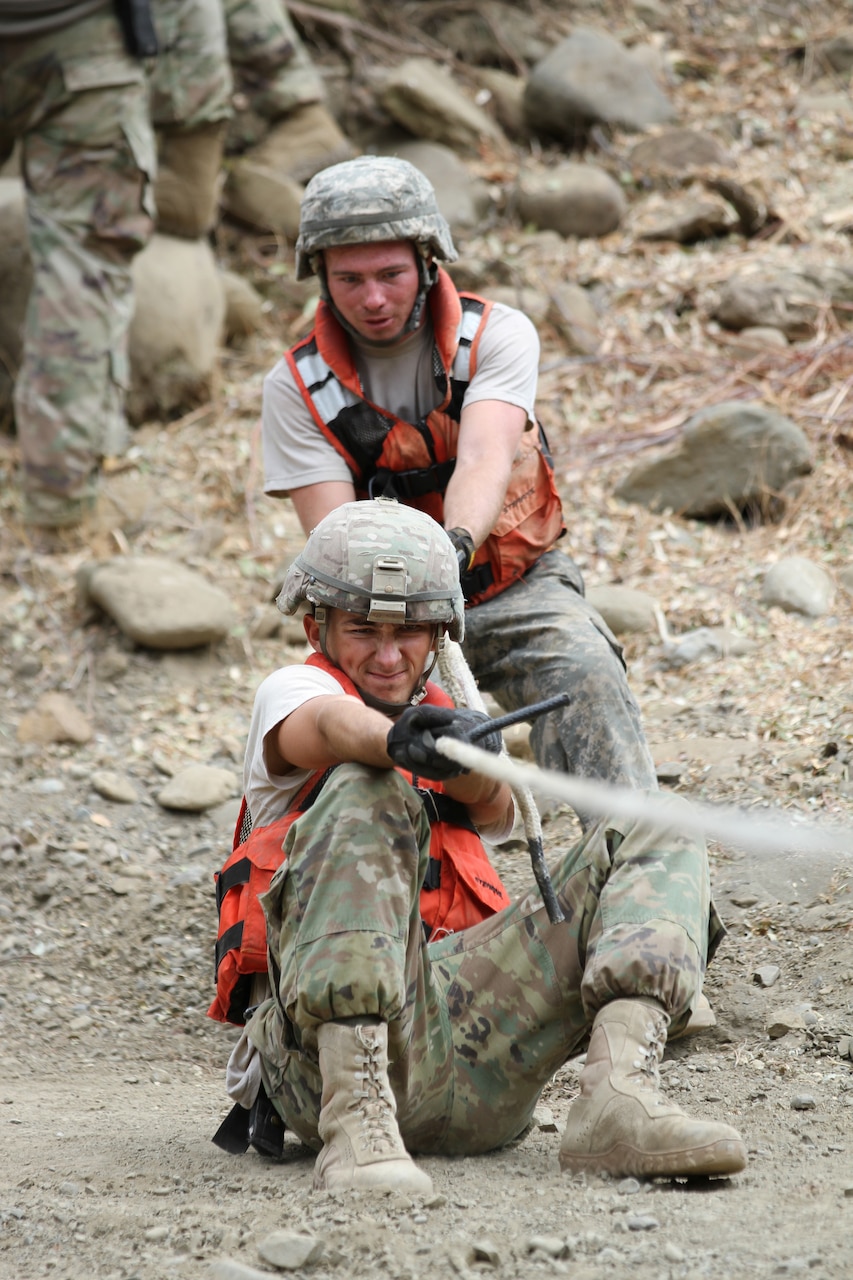 Army National Guard engineers pull a rope to position a temporary floating bridge.