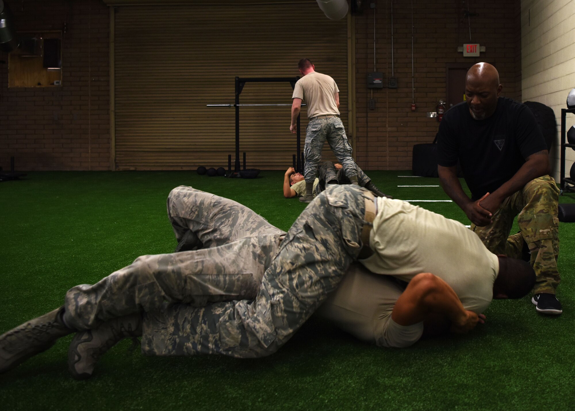 Bobby Cumby, Krav Maga instructor, observes  Senior Airman David Hightower, 56th Security Forces Squadron member, and Staff Sgt. Darics Preston, 56th Security Forces Squadron member practice choke defenses at the Tactical Integrated Training and Nutrition Arena July 12, 2018, at Luke Air Force Base, Ariz.