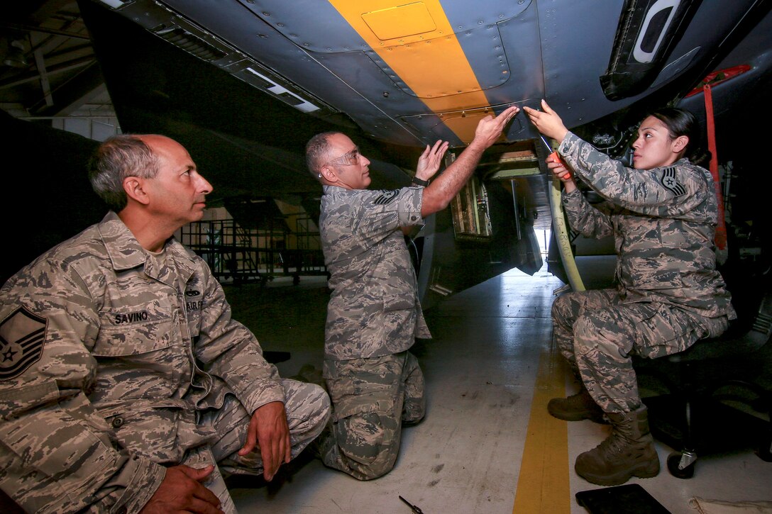 An airman observes as other airmen remove an antenna from a KC-135R Stratotanker.