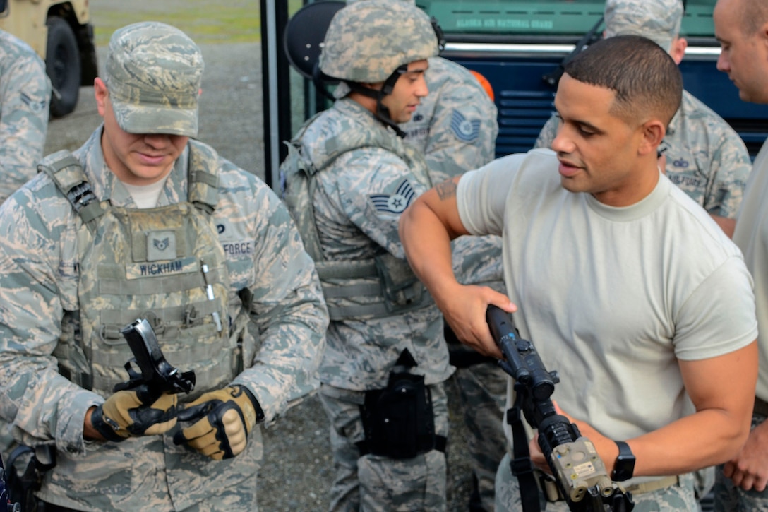 An airman retrieves a weapon from a team member before a combat patrol exercise.