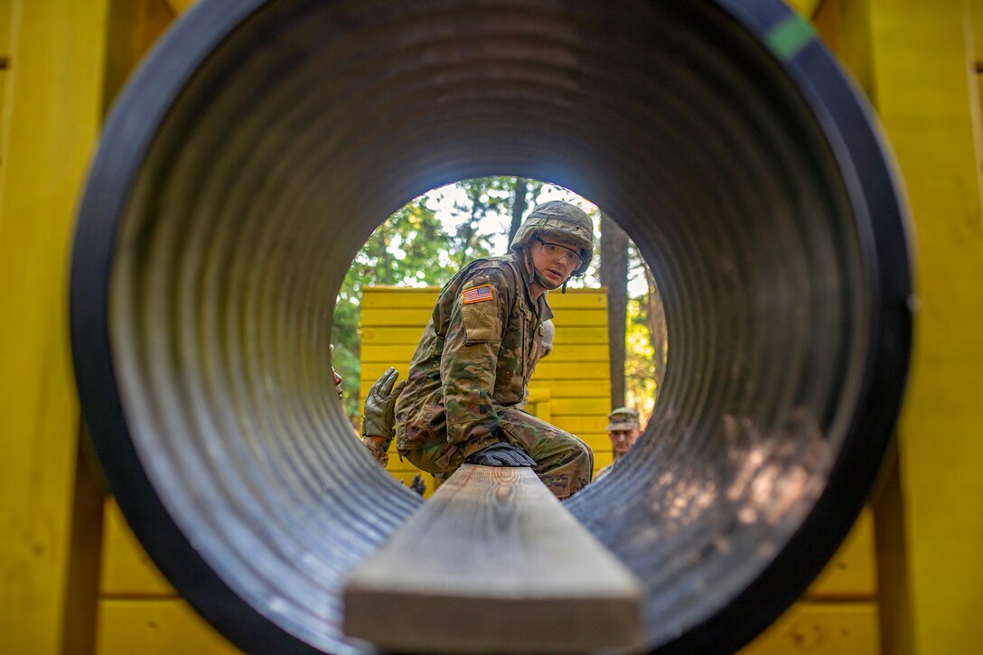 A soldier sits on a plank of wood looking through tunnel.