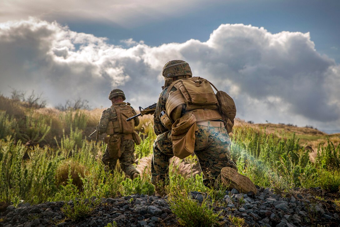 Marines kneel at a base of a hill.