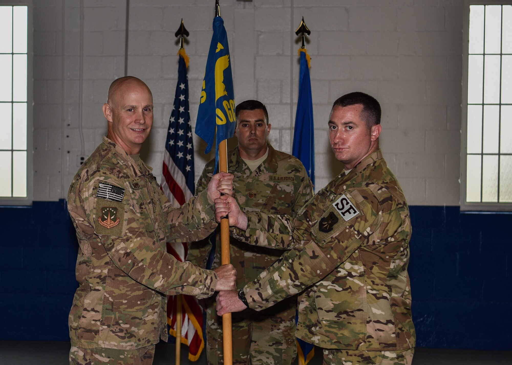 Colonel John Grimm, 90th Security Forces Group commander, passes the guidon to Maj. David Ratté, 90th Ground Combat Training Squadron commander, during the 90th GCTS change of command ceremony July 16, 2018, in Building 11 on Camp Guernsey, Wyo. The ceremony signified the transition of command from Maj. Kristen Cangelosi to Ratté. (U.S. Air Force photo by Airman 1st Class Braydon Williams)