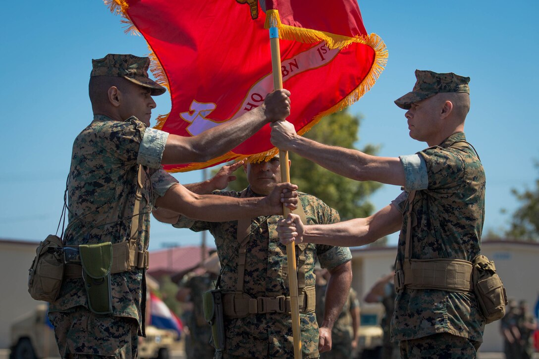 U.S. Marine Corps Maj. Arun Shankar, left, the incoming commanding officer of Headquarters Battalion (HQBN), 1st Marine Division (MARDIV), receives the Marine Corps flag from Col. Carlos O. Urbina, right, offgoing commanding officer of HQBN, 1st MARDIV, during a change of command ceremony at Marine Corps Base Camp Pendleton, Calif., June 19, 2018.
