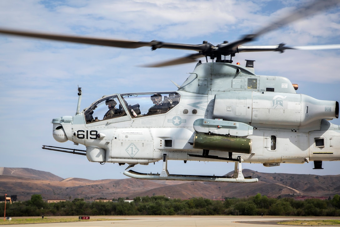 Marines hover over the flight line in an AH-1Z Viper helicopter.