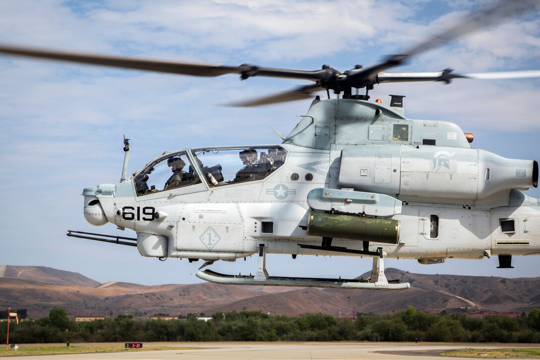 Marines hover over the flight line in an AH-1Z Viper helicopter.