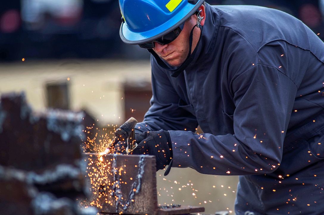 An airman leans over and cuts metal.