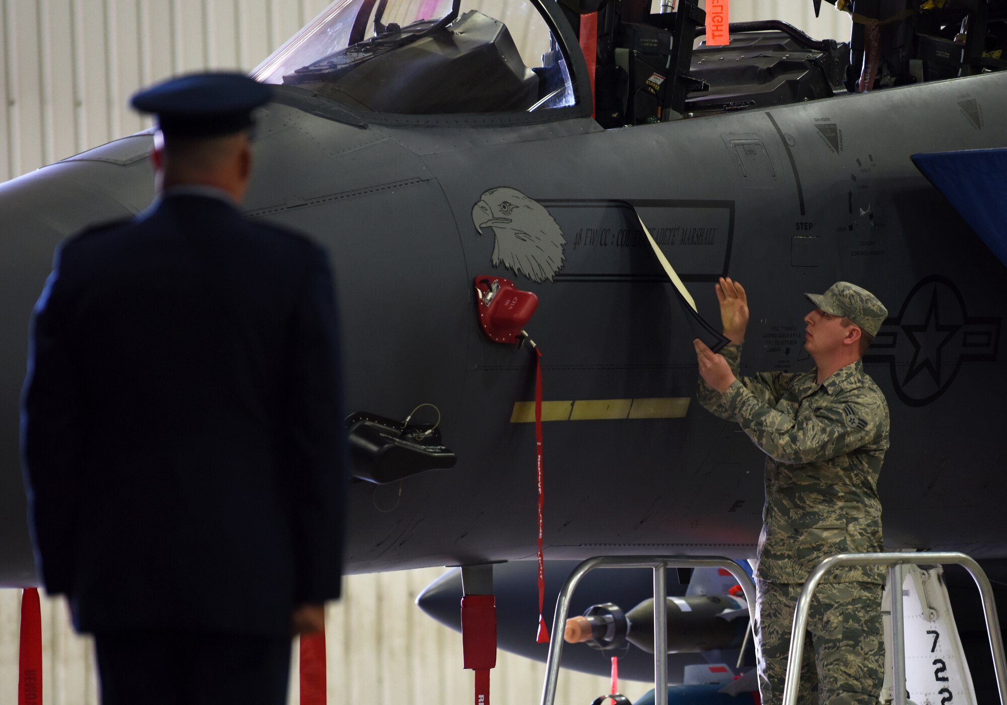 A 48th Fighter Wing Airman unveils Col. William Marshall’s name on the side of an F-15E Strike Eagle during the wing change of command ceremony at Royal Air Force Lakenheath, England, July 16, 2018. As is tradition, each Liberty Wing aircraft bears the name of the assigned aircrew on the fuselage. (U.S. Air Force photo by Staff Sgt. Alex Fox Echols III)