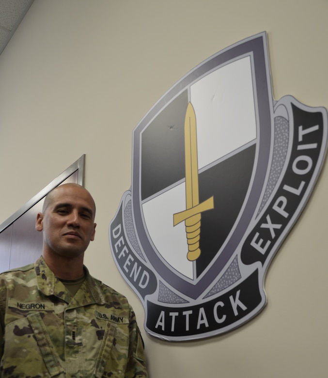 A soldier stands near a wall displaying a military crest.