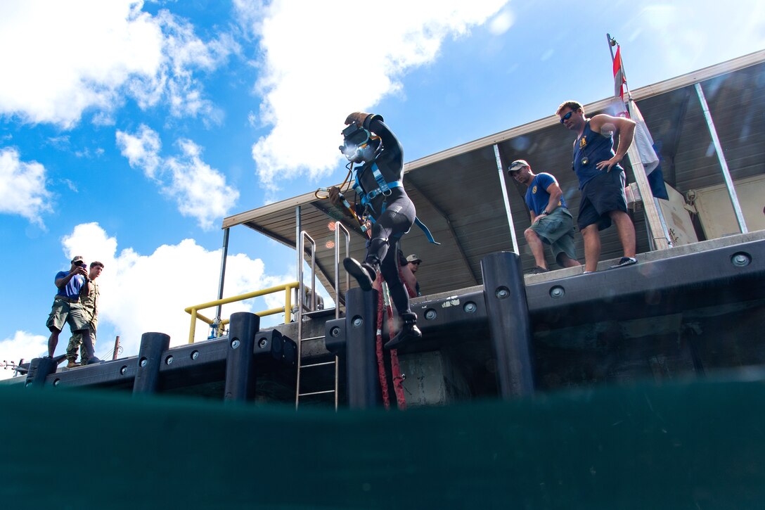 A sailor leaps into the water before conducting underwater welding operations.