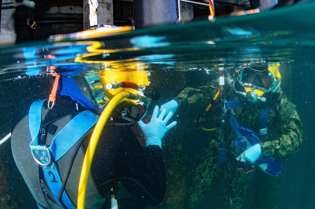 Sailors perform in-water leak checks during underwater welding operation.