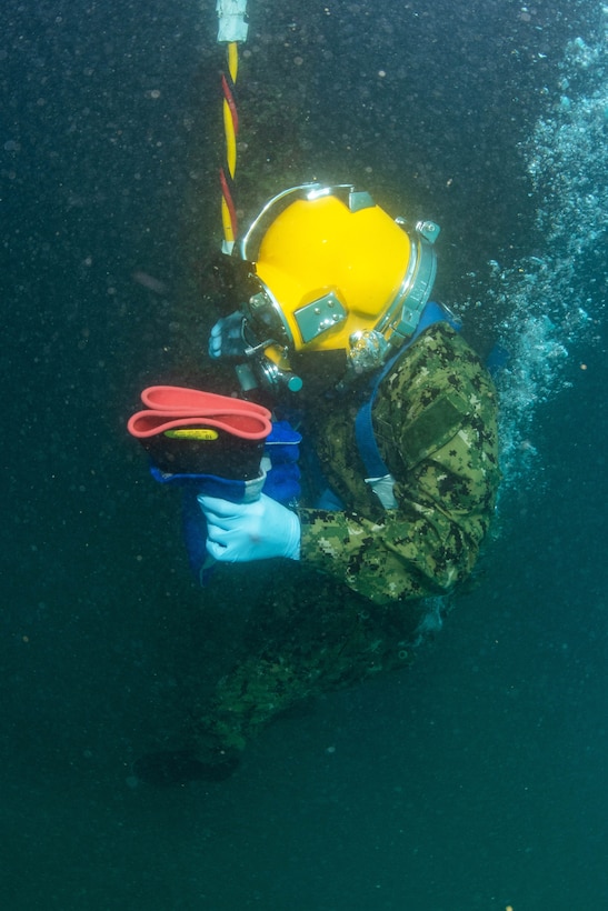 A sailor descends in the water column for underwater welding operation.