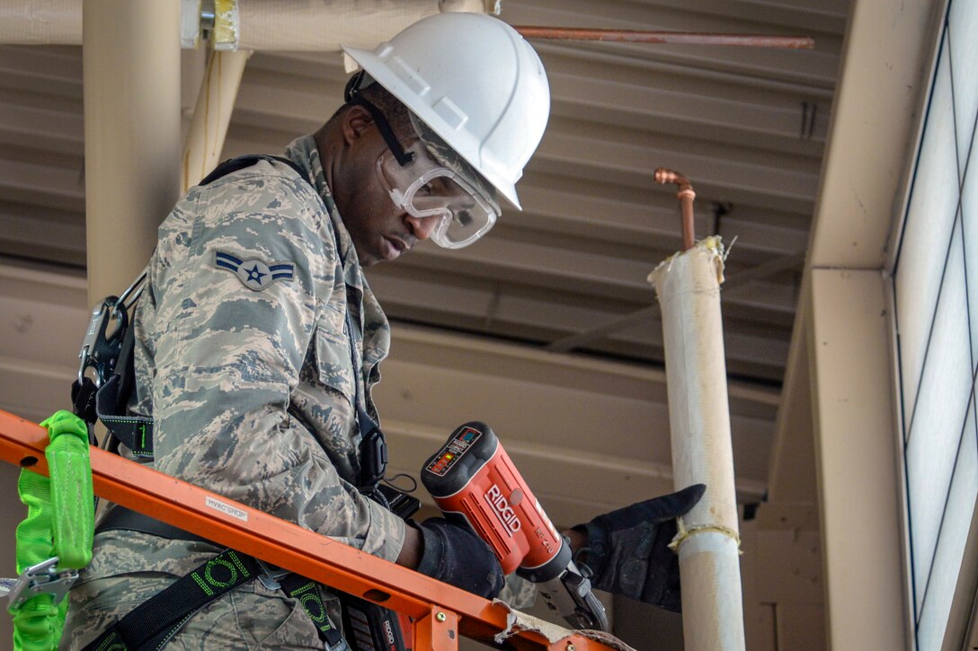 An airman wearing protective gear works on a pipe.