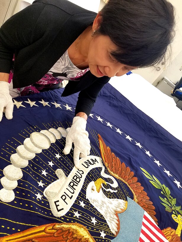 DLA Troop Support Clothing and Textiles embroidery specialist Linda Le inspects the only 49-star presidential flag made during a visit from presidential flag collectors Chuck and Donna Douglas in late June in Philadelphia. DLA embroiders are the sole authorized producers of the current 50-star presidential and vice presidential flags.
