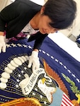 DLA Troop Support Clothing and Textiles embroidery specialist Linda Le inspects the only 49-star presidential flag made during a visit from presidential flag collectors Chuck and Donna Douglas in late June in Philadelphia. DLA embroiders are the sole authorized producers of the current 50-star presidential and vice presidential flags.