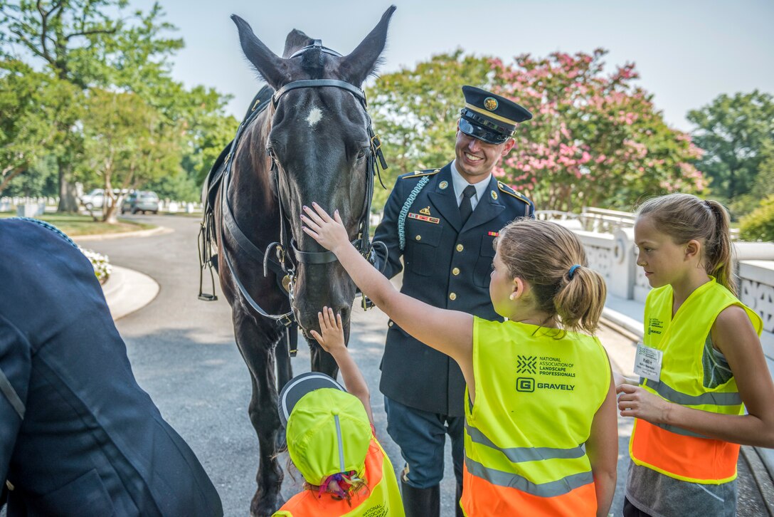 Children pet a horse while a soldier holds the reins.