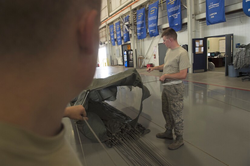 U.S. Air Force Senior Airmen Joshua Harris, an aerial operations apprentice assigned to the 97th LRS, and U.S. Air Force Senior Airman William Plate, an aerial operations apprentice assigned to the 97th LRS inspect a parachute after a recent air drop, July 11, 2018, at Altus Air Force Base, Okla.