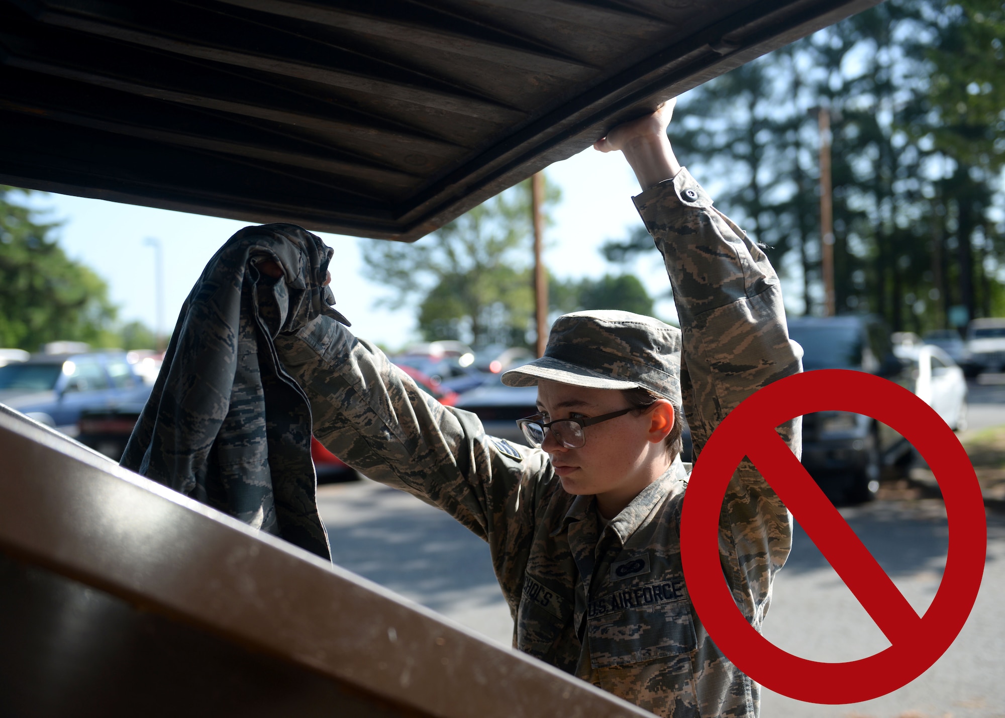 A woman in the Airman Battle Uniform is putting a blouse in to a dumpster.