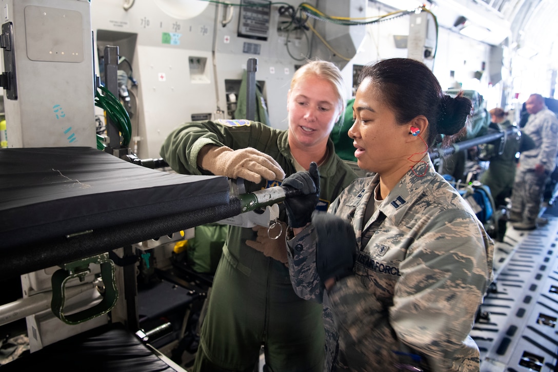 U.S. Air Force Master Sgt. Michelle Geers, an aeromedical evacuation technician from the 315th Aeromedical Evacuation Squadron, demonstrates the locking mechanism for a litter used aboard a U.S. Air Force C-17 Globemaster III aircraft with Capt. Louisealbertine Sarabosing, a clinical nurse with the 624th Aeromedical Staging Squadron, at U.S. Coast Guard Air Station Barbers Point, Hawaii, July 10, 2018, during Pacific Lifeline 2018.