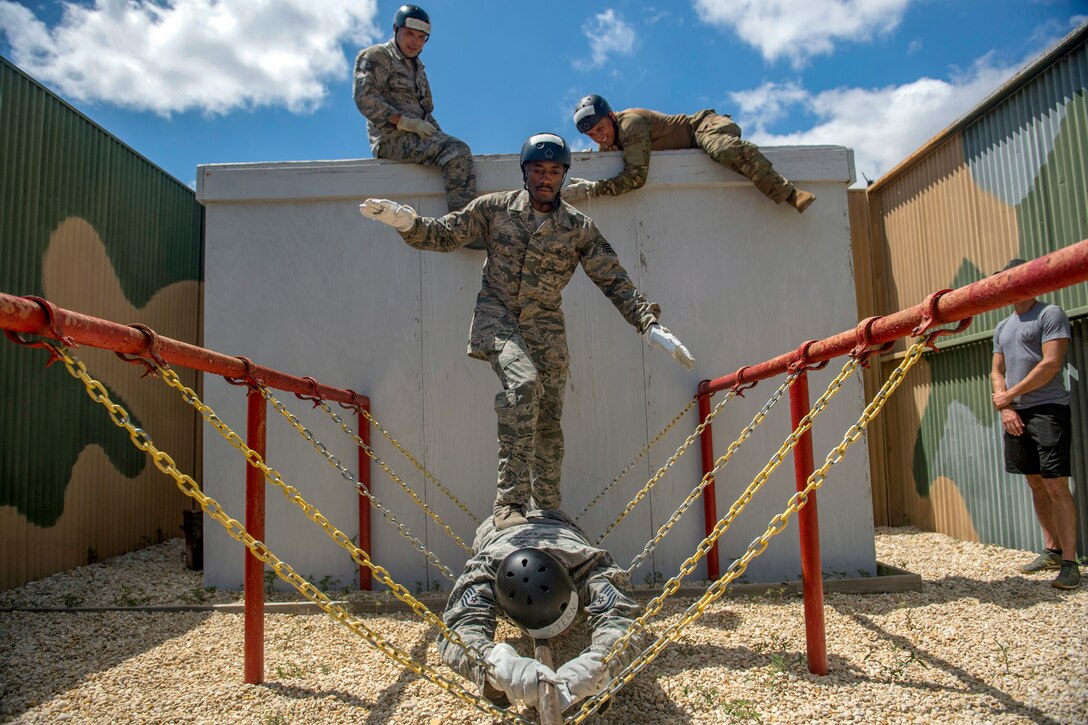 An airman walks across the back of another airman, who's lying on a chain link obstacle.