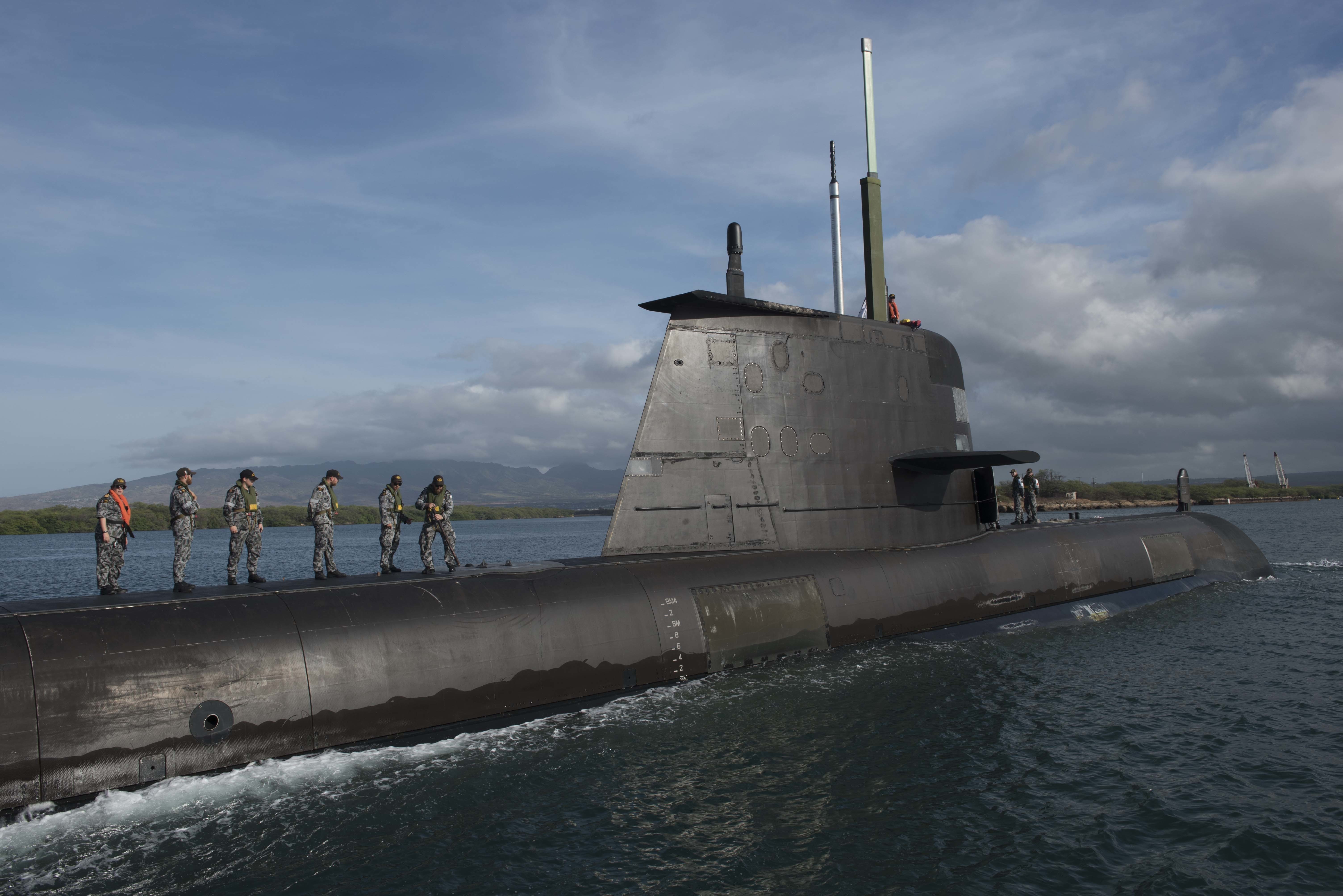 The crew of the Royal Australian Navy submarine HMAS Rankin stand on top of submarine while in the water.