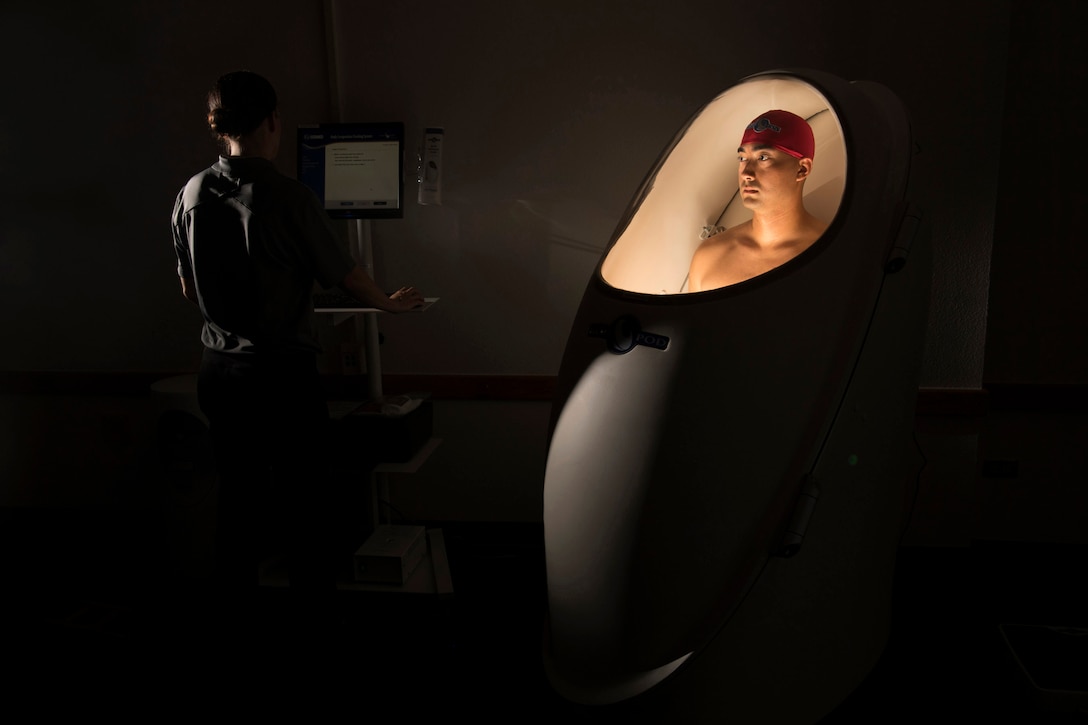 An airman stands in a lighted pod during a body composition test.