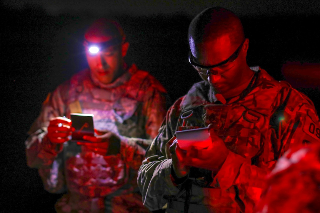 Two soldiers look at notepads at night.