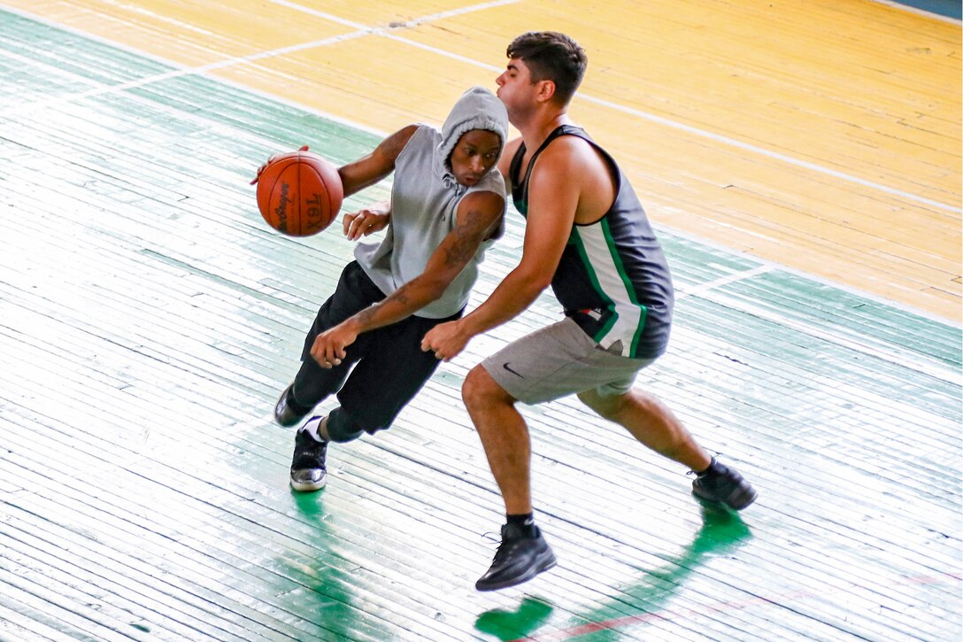 Two service members play basketball.