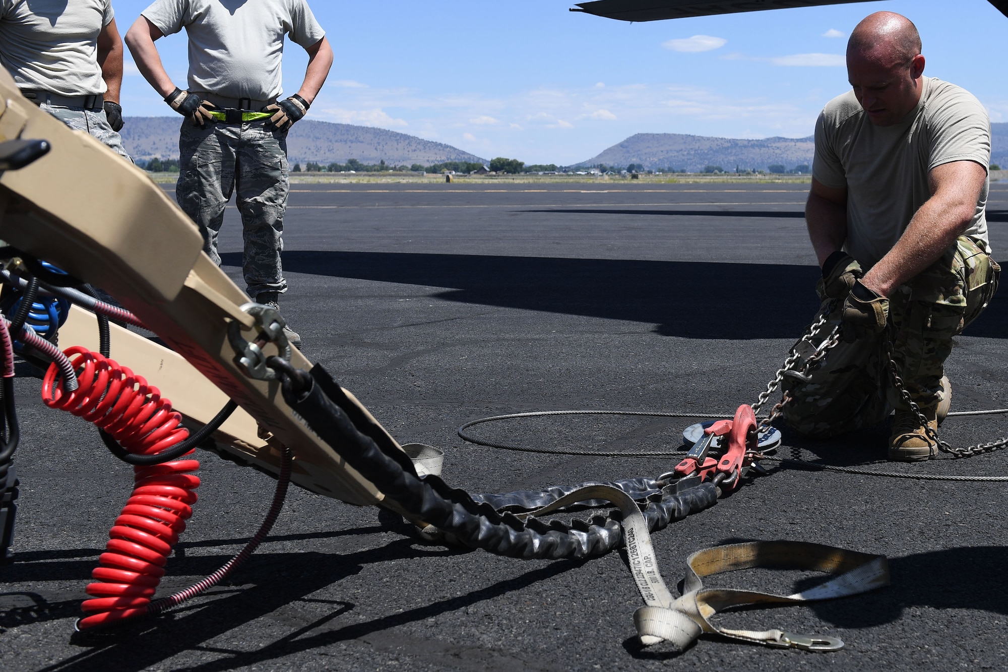 Airman connects cable from plane to chains of object.