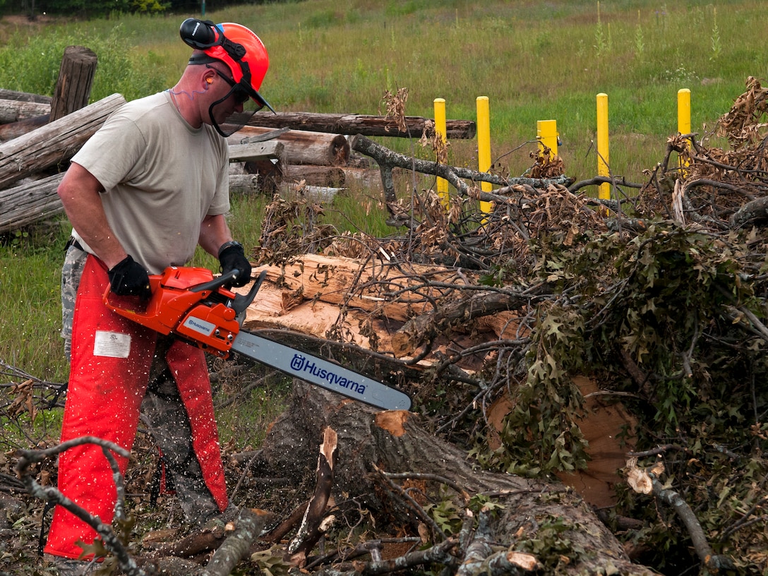 Airman uses a chainsaw to cut a fallen tree.