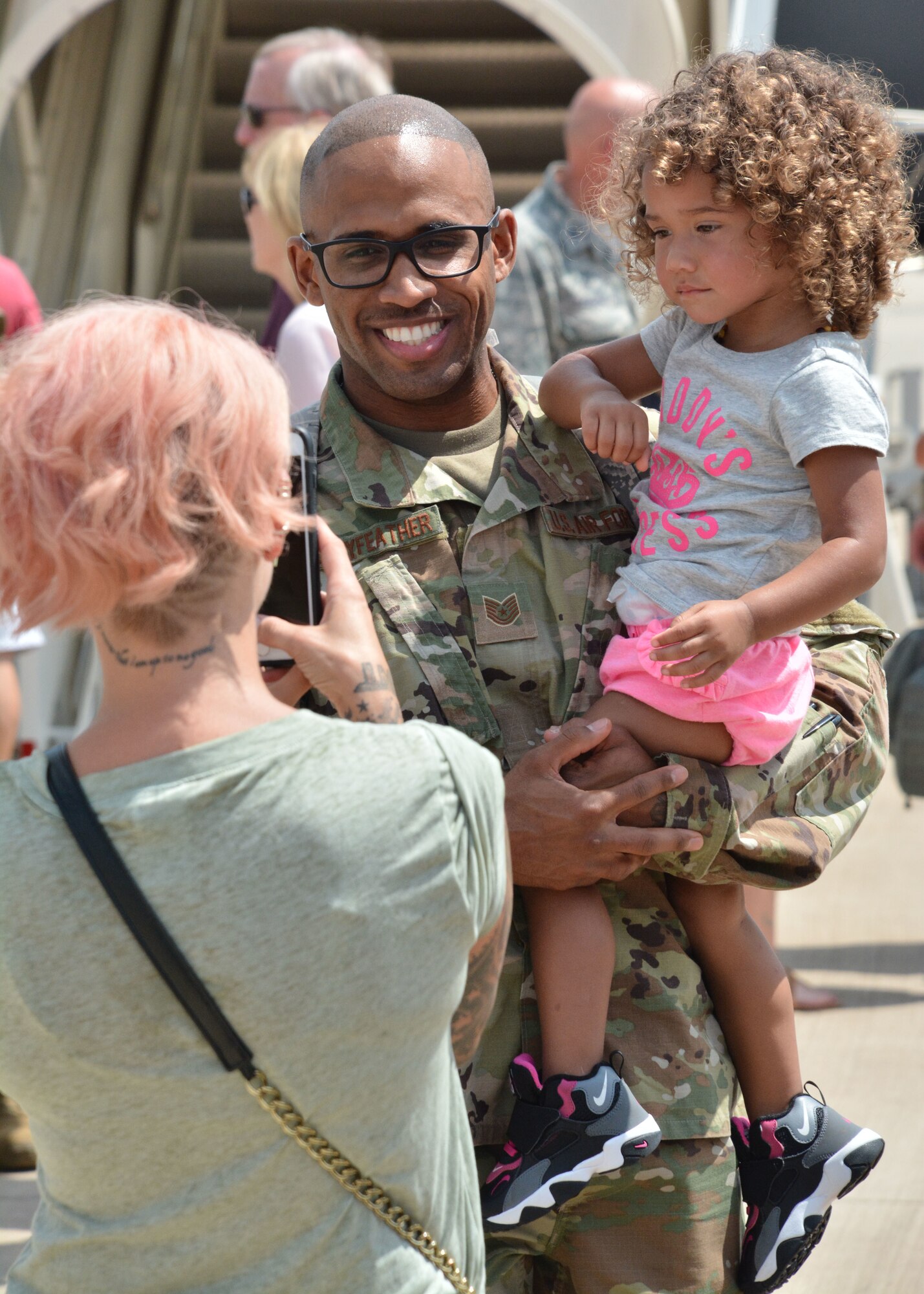 U.S. Air Force Tech. Sgt. Leon Pennyfeather, a combat crew communications technician with the 507th Operations Support Squadron at Tinker Air Force Base, Okla., holds his daughter while his wife snaps a photograph upon returning from deployment July 7, 2018. More than 100 Reserve Citizen Airmen from the 507th ARW at Tinker AFB deployed to Incirlik Air Base, Turkey, in support of air operations. (U.S. Air Force photo by Master Sgt. Grady Epperly)