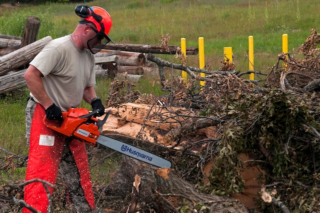 An Airman uses a chainsaw to cut debris.