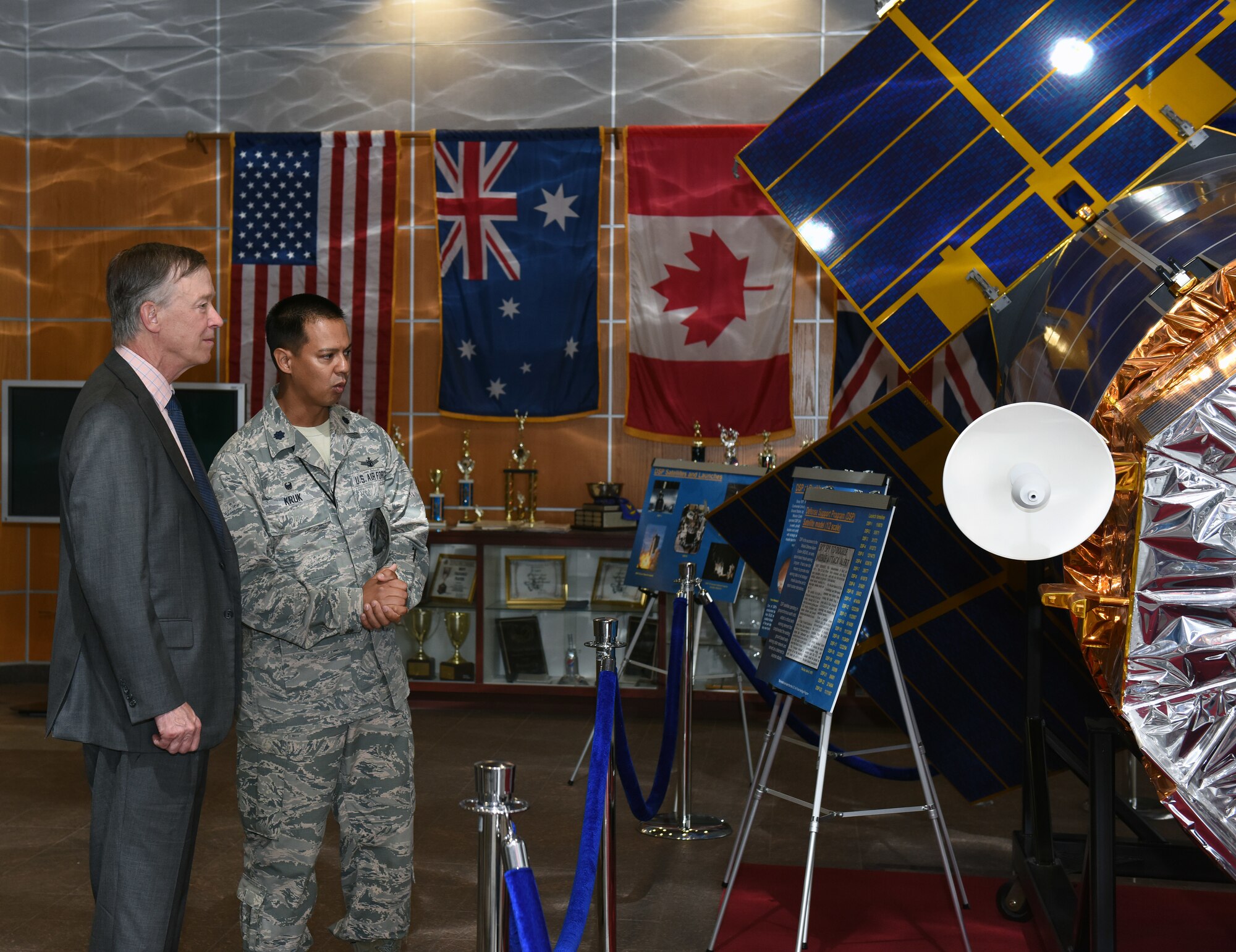 Gov. John Hickenlooper of Colorado, far left, receives a briefing from Lt. Col. Michael Kruk, 11th Space Warning Squadron commander, on the Space Based Infrared System in the Mission Control Station lobby at Buckley Air Force Base, Colorado, July 17, 2018