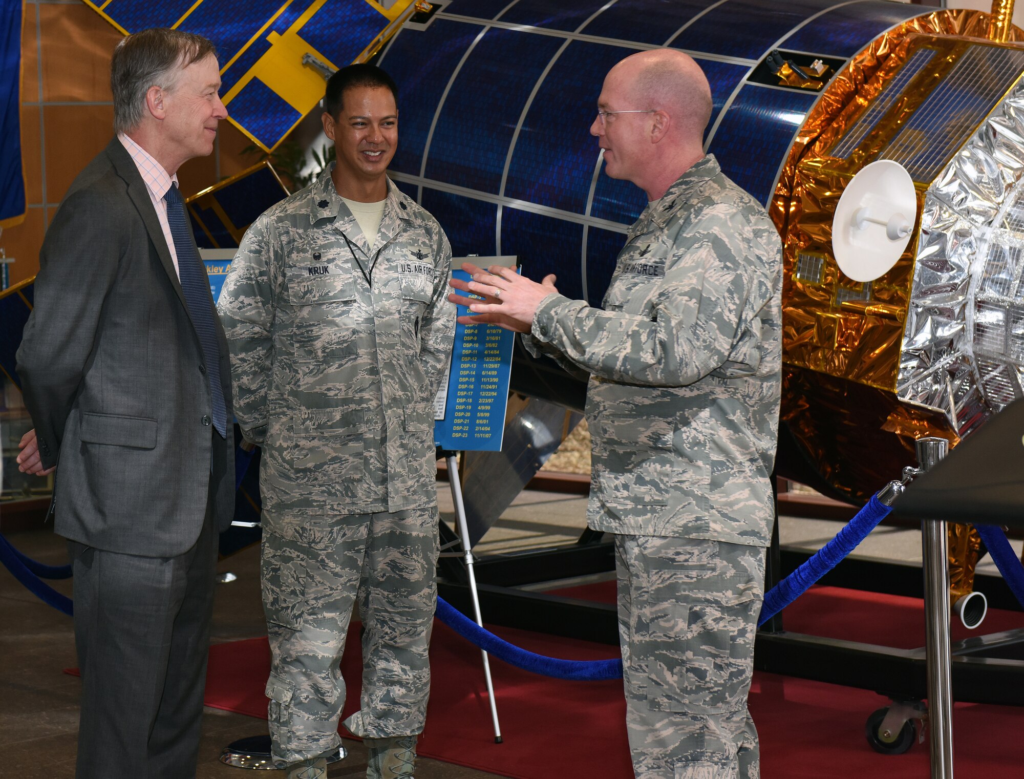 Gov. John Hickenlooper of Colorado, far left, receives a briefing from Col. Troy Endicott, far right, 460th Space Wing commander, and Lt. Col. Michael Kruk, 11th Space Warning Squadron commander, on the Space Based Infrared System in the Mission Control Station lobby at Buckley Air Force Base, Colorado, July 17, 2018.