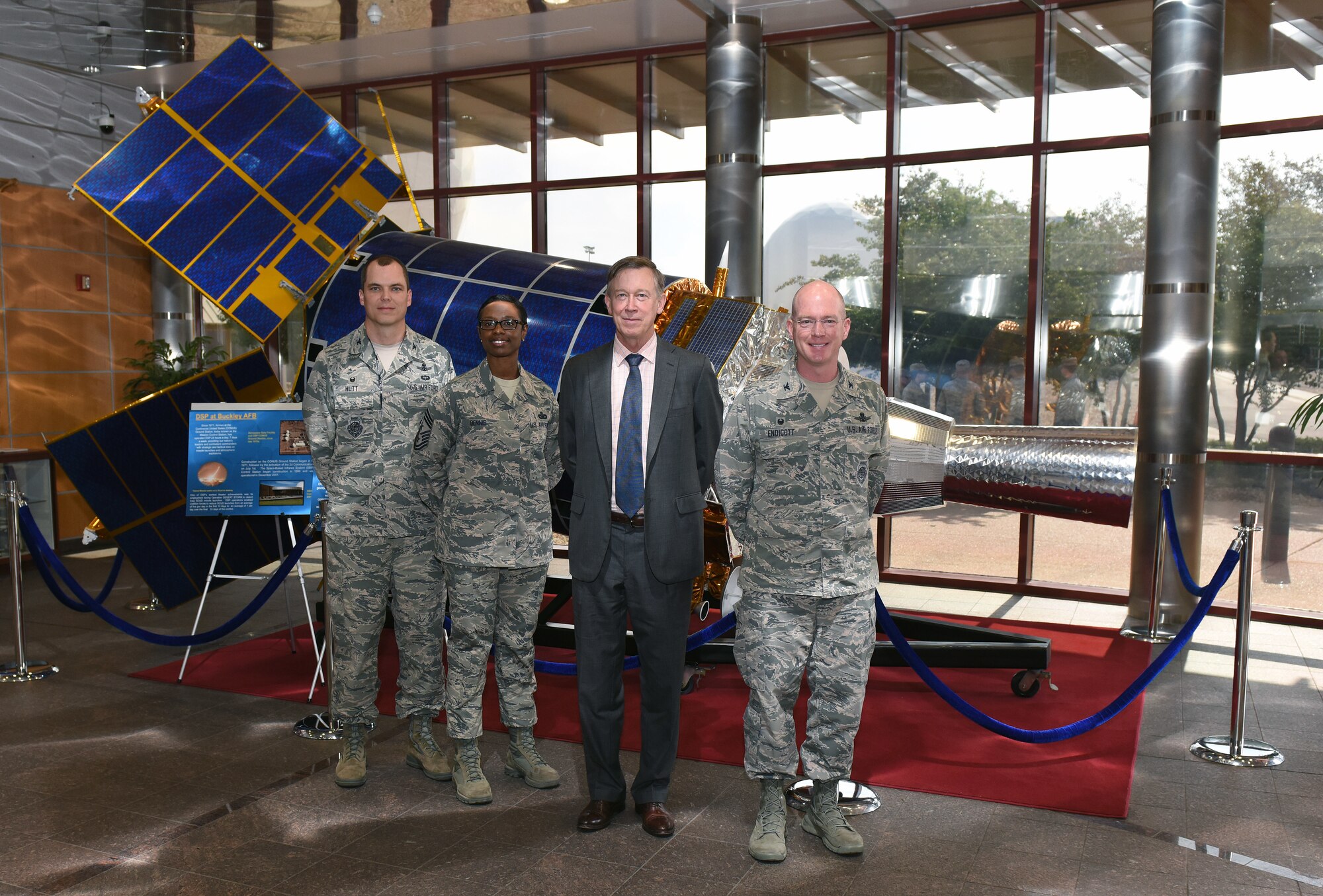 From left to right, Col. Robert Hutt, 460th Operations Group commander, Chief Master Sgt. Tamar Dennis, 460th Space Wing incoming command chief, Gov. John Hickenlooper of Colorado, and Col. Troy L. Endicott, the 460th Space Wing commander, stand for a group photo in front of the Space Based Infrared System in the Mission Control Station lobby at Buckley Air Force Base, Colorado, July 17, 2018.
