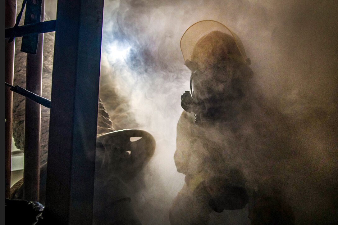A sailor, shown in silhouette, moves though a smoky area aboard a ship.
