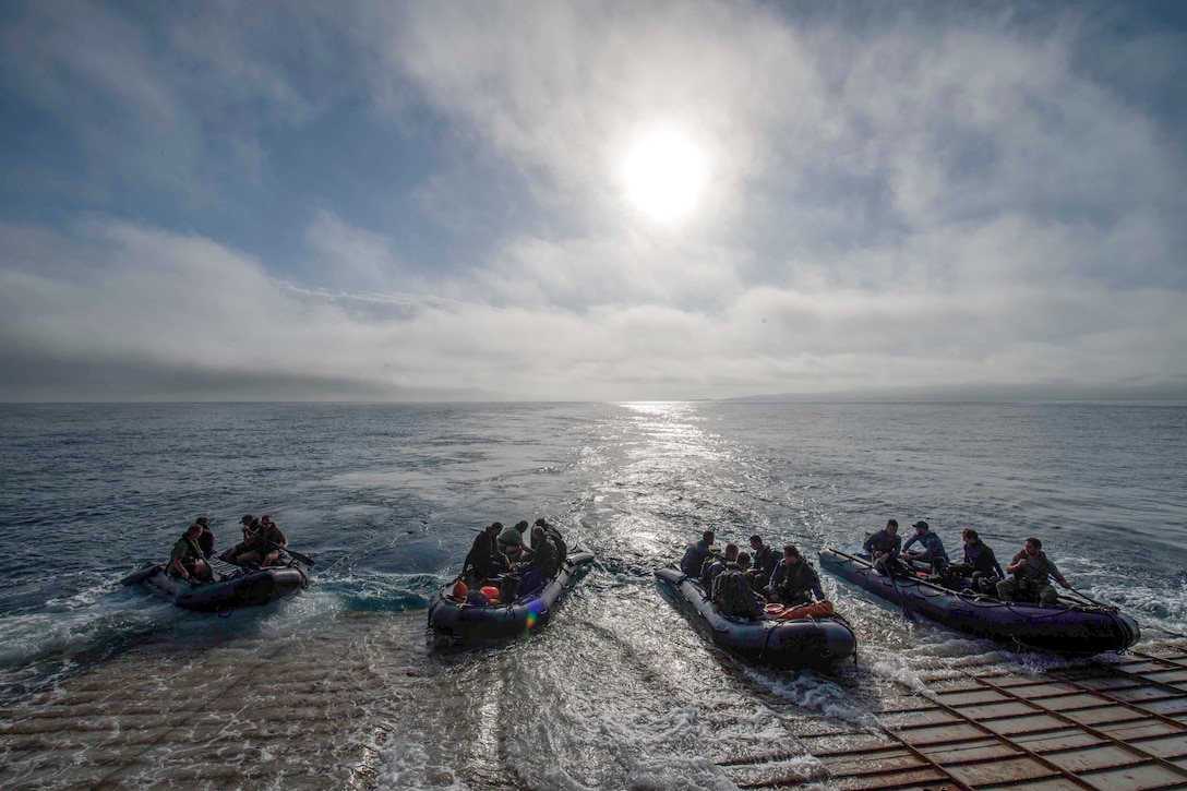 Four small boats enter the water from the back of a ship.