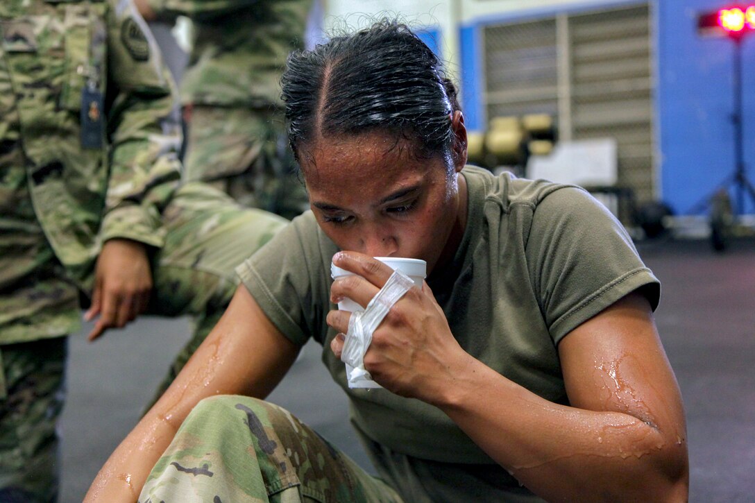 A soldier sits on the ground drinking water.