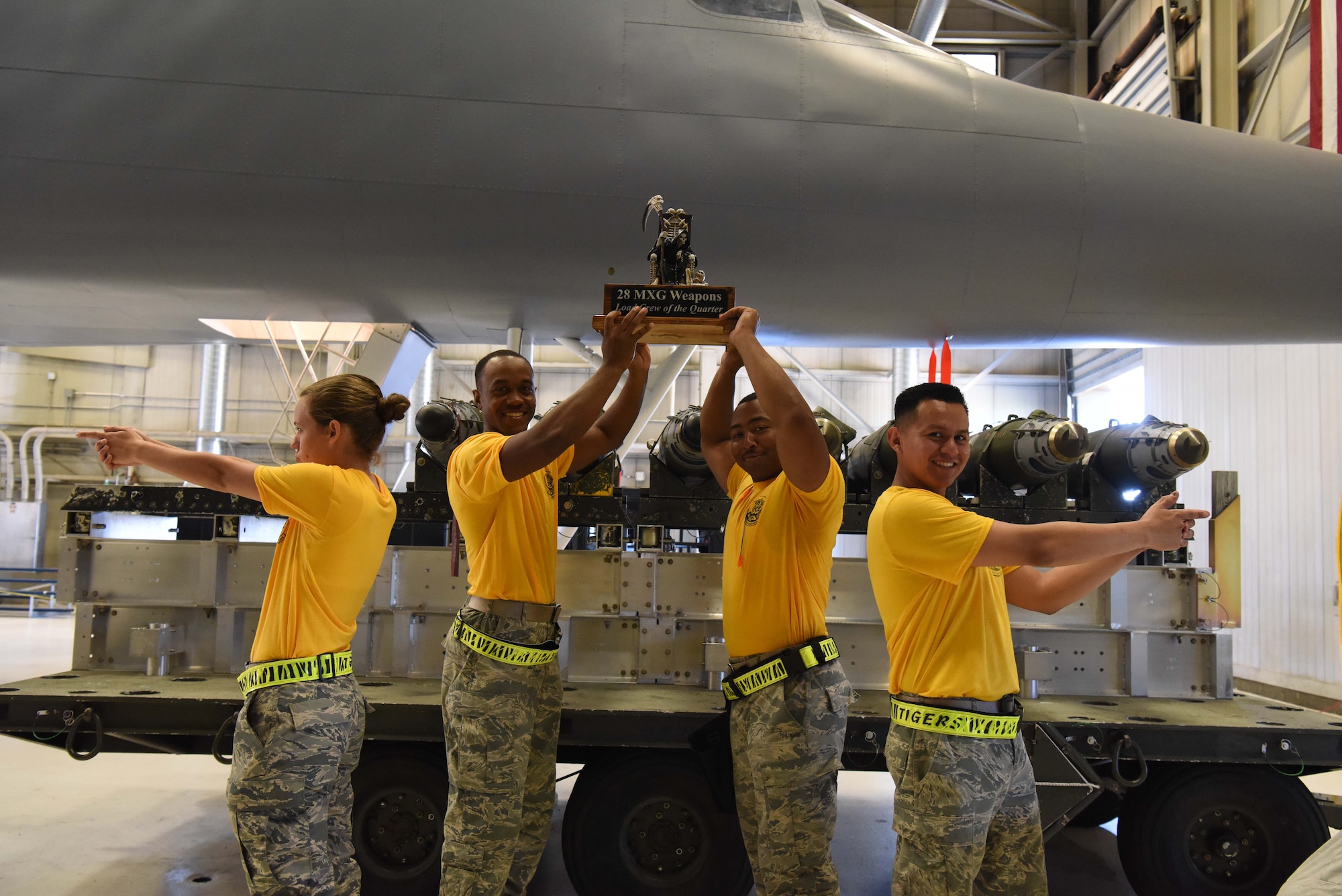 Members from the 37th Aircraft Maintenance Unit hold a trophy in the Load Crew Training Facility after winning a load competition at Ellsworth Air Force Base, S.D., July 13, 2018. Two teams of four competed to see who the best AMU of the quarter was by seeing who could load bombs the fastest and with the fewest errors. (U.S Air Force photo by Airman 1st Class Thomas Karol)