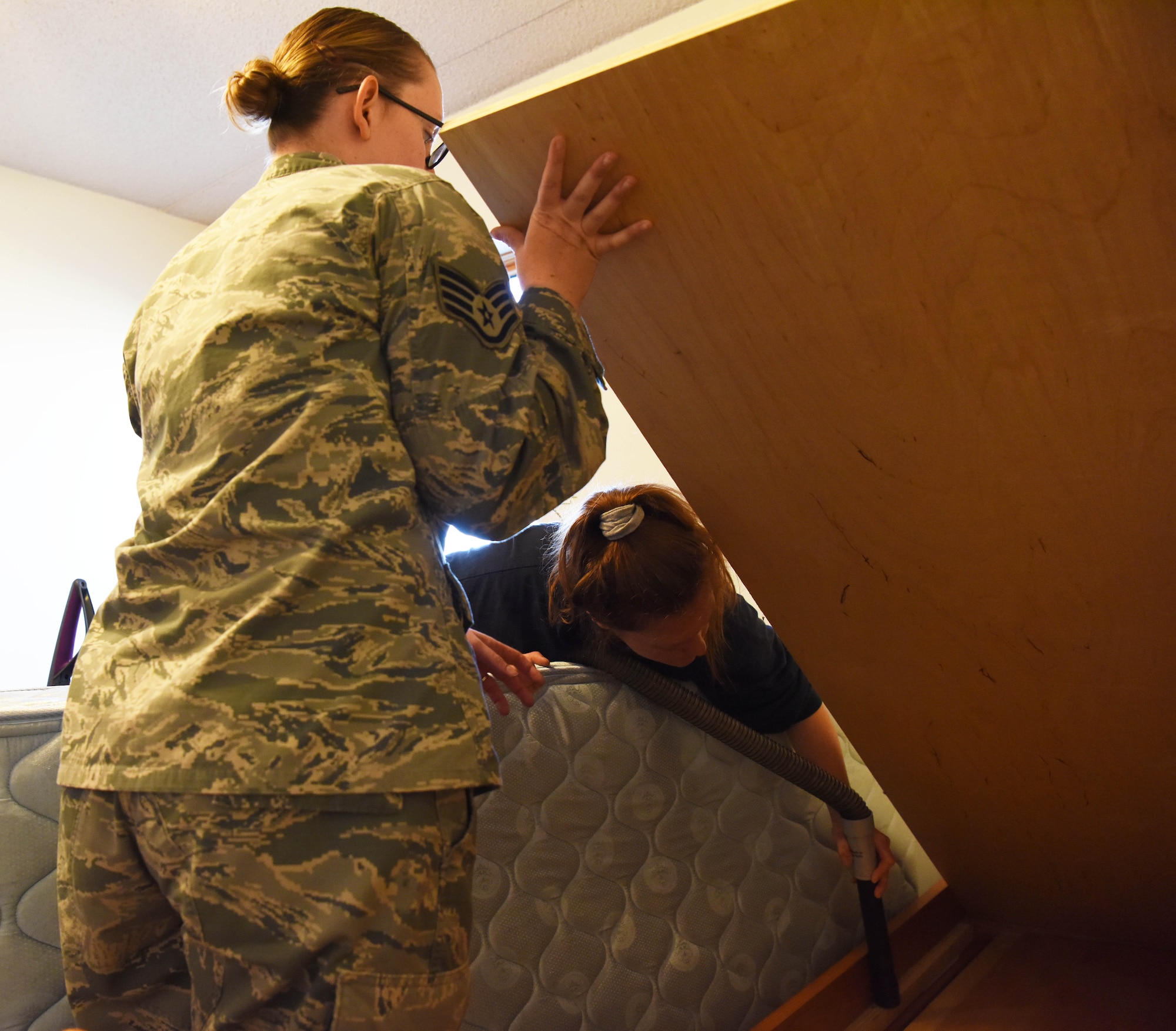 Staff Sgt. Hailey Staker, an Airman dorm leader, lifts a bed frame so Airman 1st Class Casi Smith, a 28th Security Forces response force leader, can clean under it at Ellsworth Air Force Base, S.D., July 17, 2018. Airmen are responsible for cleaning their rooms before they out-process and move to a new home. (U.S. Air Force photo by Airman 1st Class Thomas Karol)